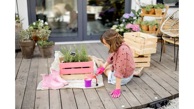 Person gestaltet DIY-Projekt mit bemalter Holzkiste auf der Terrasse.
