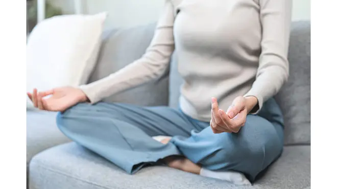 Person meditiert entspannt auf dem Sofa.