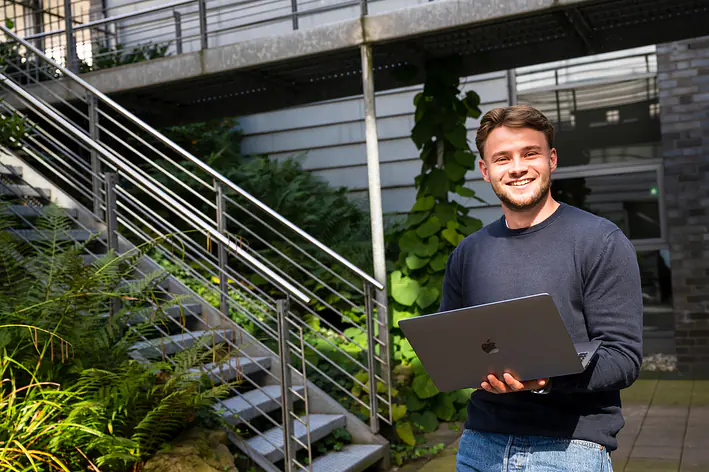 Auszubildender sitzt im Außenbereich des Büros mit Laptop in der Hand