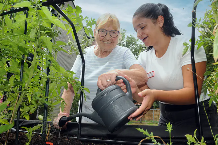 Auszubildende hilft Seniorin beim Blumen gießen