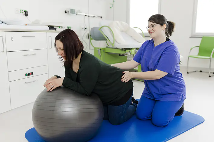 Foto einer Schwangeren, die auf einem Ball liegt und einer Hebamme