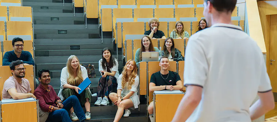 Studierende im Hörsaal unterhalten sich mit einem Dozenten