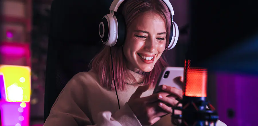 Studierende sitzt vor Podcast Mikrophon und hat ihr Handy in der Hand