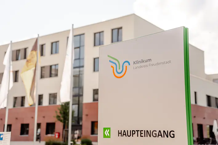 Foto vom Gebäude und der Außenansicht sowie dem Schild zum Haupteingang