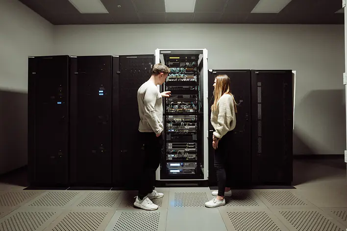 Arbeiten im Serverraum Zwei Personen stehen vor geöffneten Serverschränken in einem Rechenzentrums- oder Technikraum und betrachten die darin verbaute Hardware.