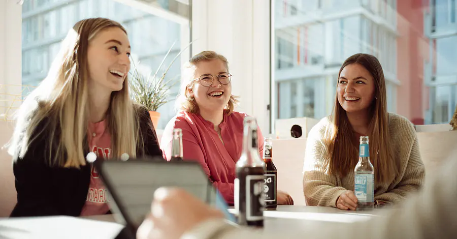 Teammeeting Mehrere Personen sitzen an einem Besprechungstisch in einem lichtdurchfluteten Raum. Auf dem Tisch stehen Getränke, während die Gruppe gemeinsam an einer Besprechung teilnimmt.