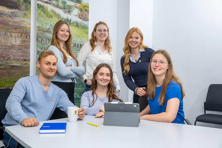 Eine Gruppe Auszubildender, die am Tisch sitzen und in die Kamera lächeln.