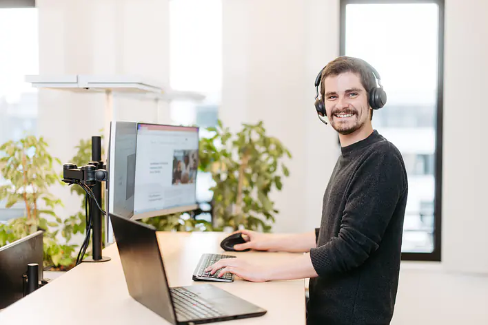 Mann steht vor Laptop und Bildschirm am Schreibtisch