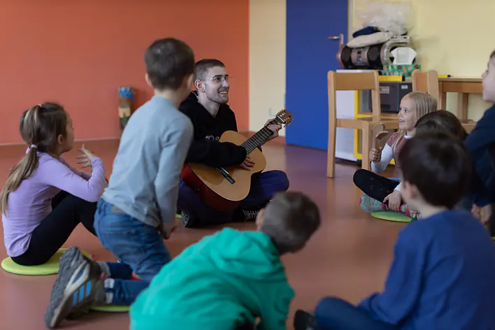 Ein Mann spielt mit Kindern gemeinsam Gitarre.